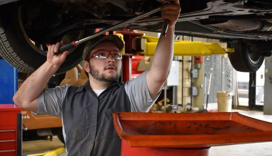 student in auto shop working on diesel engine while 车 is on a lift